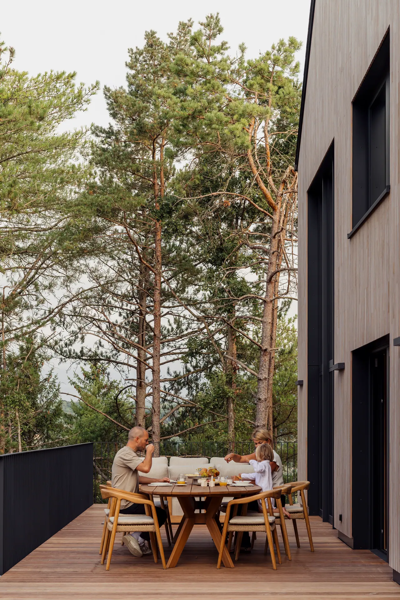 Een gezin ontbijt op het terras naast de houten gevel van Les Terrasses de Durbuy
