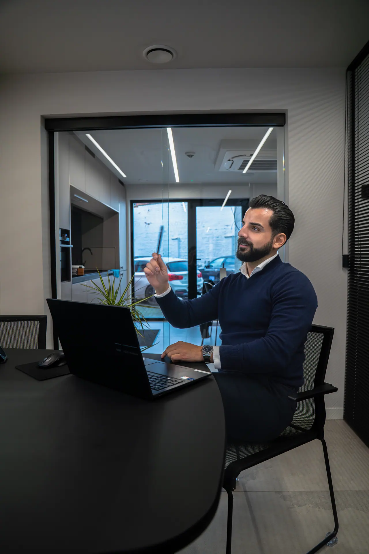 Wat kost een AI-chatbot: een man aan een laptop in een glazen vergaderruimte legt het uit, met zijn hand in de lucht