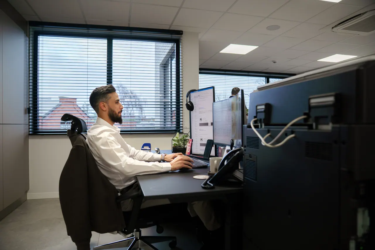 Wat kost een website per jaar: een man rekent het na aan een bureau met twee schermen in een licht kantoor
