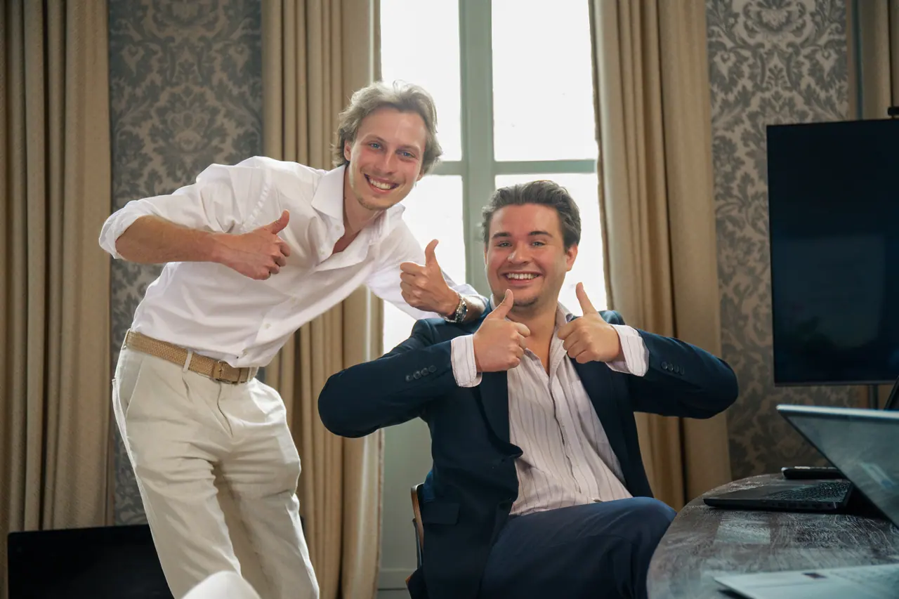 Twee collega's van VBS lachen met de duimen omhoog in ons kantoor